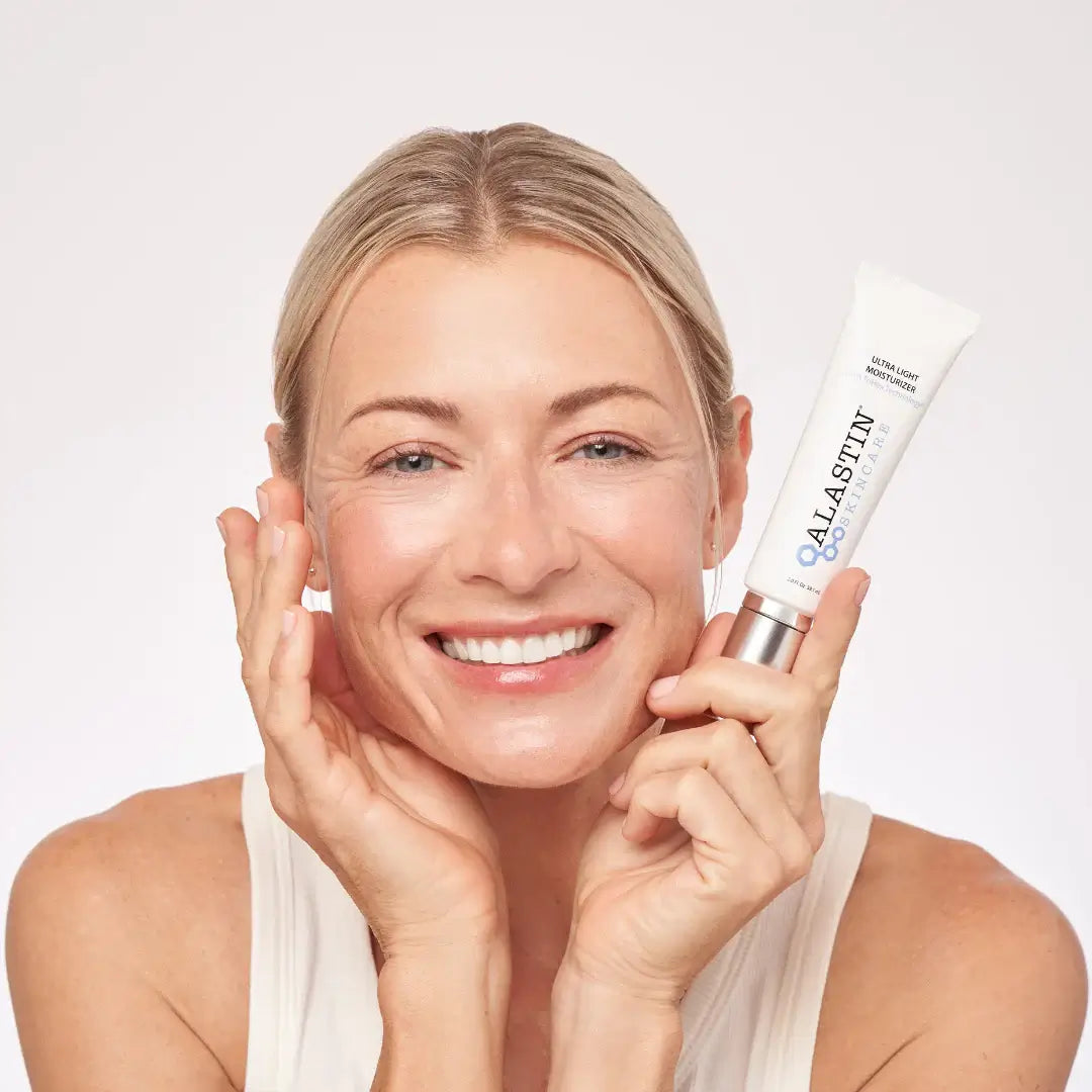 Alastin Ultra Light Moisturizer in hand, showcasing hydration and calm skin with a radiant smile.