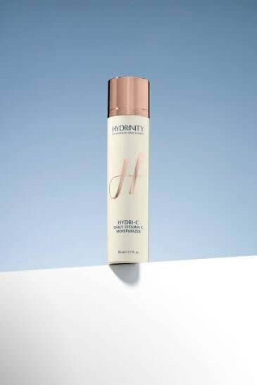 Hydri-C Vitamin C Moisturizer bottle on a white surface against a light blue background.