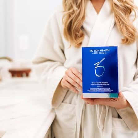 Woman in robe holding ZO Daily Skincare Program box in a bright bathroom setting.